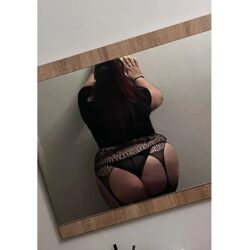 Back view of a person wearing a black top and lace lingerie with a garter belt, standing in front of a wall mirror.