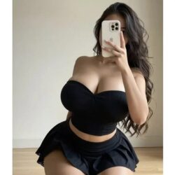 Woman in a black strapless crop top and black mini skirt taking a mirror selfie with a smartphone.