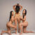 Three women in beige lingerie posing in a studio; one stands center with hands in her hair, the others kneel beside her, watermark across the image.