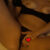 Topless person lying on a bed with legs apart; hand resting near the genital area, censored by a red pixel heart.
