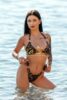 Woman in a leopard-print bikini standing in shallow blue water, looking at the camera.