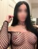 Person with long dark hair wearing a black fishnet top that reveals shoulders and chest, standing in a kitchen with a blurred face for privacy