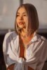 Woman with shoulder-length highlighted hair and glossy lips, wearing a knotted white shirt, looking off to the side in warm lighting, watermark visible. Woman with shoulder-length highlighted hair and glossy lips, wearing a knotted white shirt, looking off to the side in warm lighting, watermark visible.