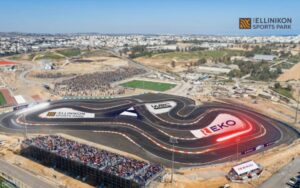 Aerial view of a winding race track at Ellinikon Sports Park with crowded grandstands and surrounding construction nearby.