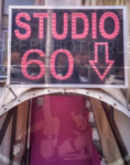 Sign reading 'STUDIO 60' in pink letters with a downward arrow, mounted above a narrow entrance with a pink-lit interior visible below.