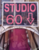 Sign reading 'STUDIO 60' in pink letters with a downward arrow, mounted above a narrow entrance with a pink-lit interior visible below.