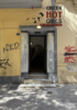 Open doorway framed by stone columns on a graffiti-covered yellow building, with a 'GREEK HOT GIRLS' ad above."