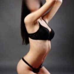 Woman in black lingerie posing on her knees in a studio, with a blurred face and gray backdrop.