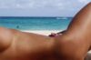 Person sunbathing on a sandy beach with turquoise sea and horizon in the background.
