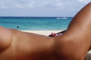 Person sunbathing on a sandy beach with turquoise sea and horizon in the background.