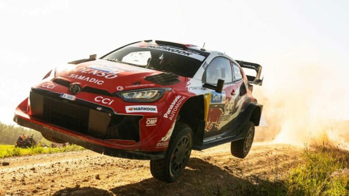 Red rally car airborne over a dirt track, dust spraying behind it. Red rally car airborne over a dirt track, dust spraying behind it.