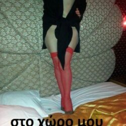 Person standing on a bed in red thigh-high stockings and a black robe, facing away; text at bottom reads 'στο χώρο μου' (in my space).
