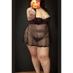 Person in sheer black lingerie with a robe, facing the camera and pointing; face covered by an emoji, standing in a doorway.