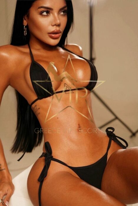 Woman in a black string bikini posing in a studio, with long dark hair and gold hoop earrings. Woman in a black string bikini posing in a studio, with long dark hair and gold hoop earrings.
